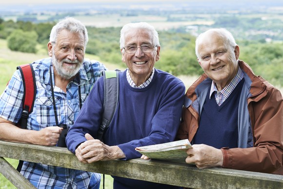 Three people outside leaning on a wooden fence.