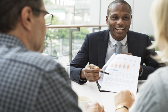 An advisor points to a chart on a piece of paper while two other people watch.