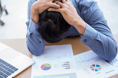 Man at desk with head down atop graph printouts