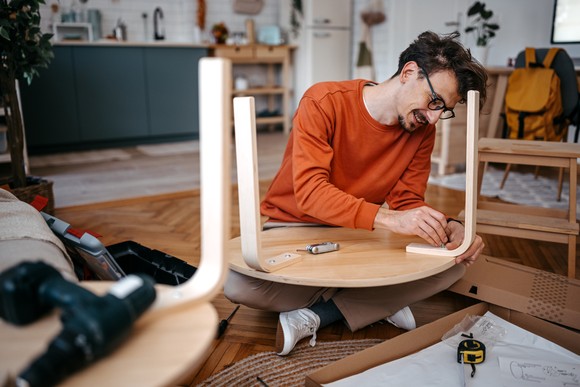 A person smiles while installing legs on a table. 