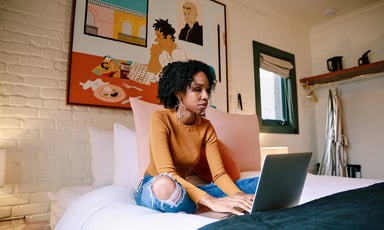 person sitting on bed with laptop open_AirBNB
