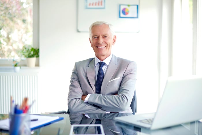 A smiling person wearing a business suit at a desk.