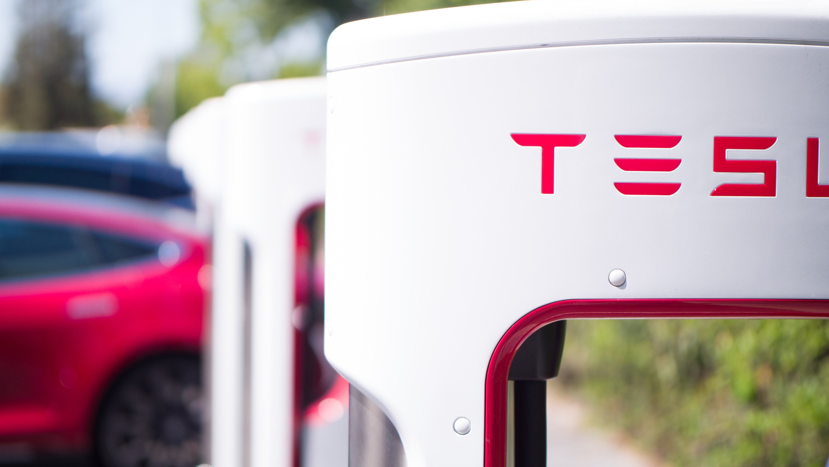 An up-close view of a Tesla supercharger, which Tesla electric vehicles parked in the background.