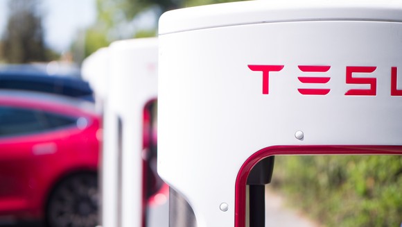 An up-close view of a Tesla supercharger, which Tesla electric vehicles parked in the background.