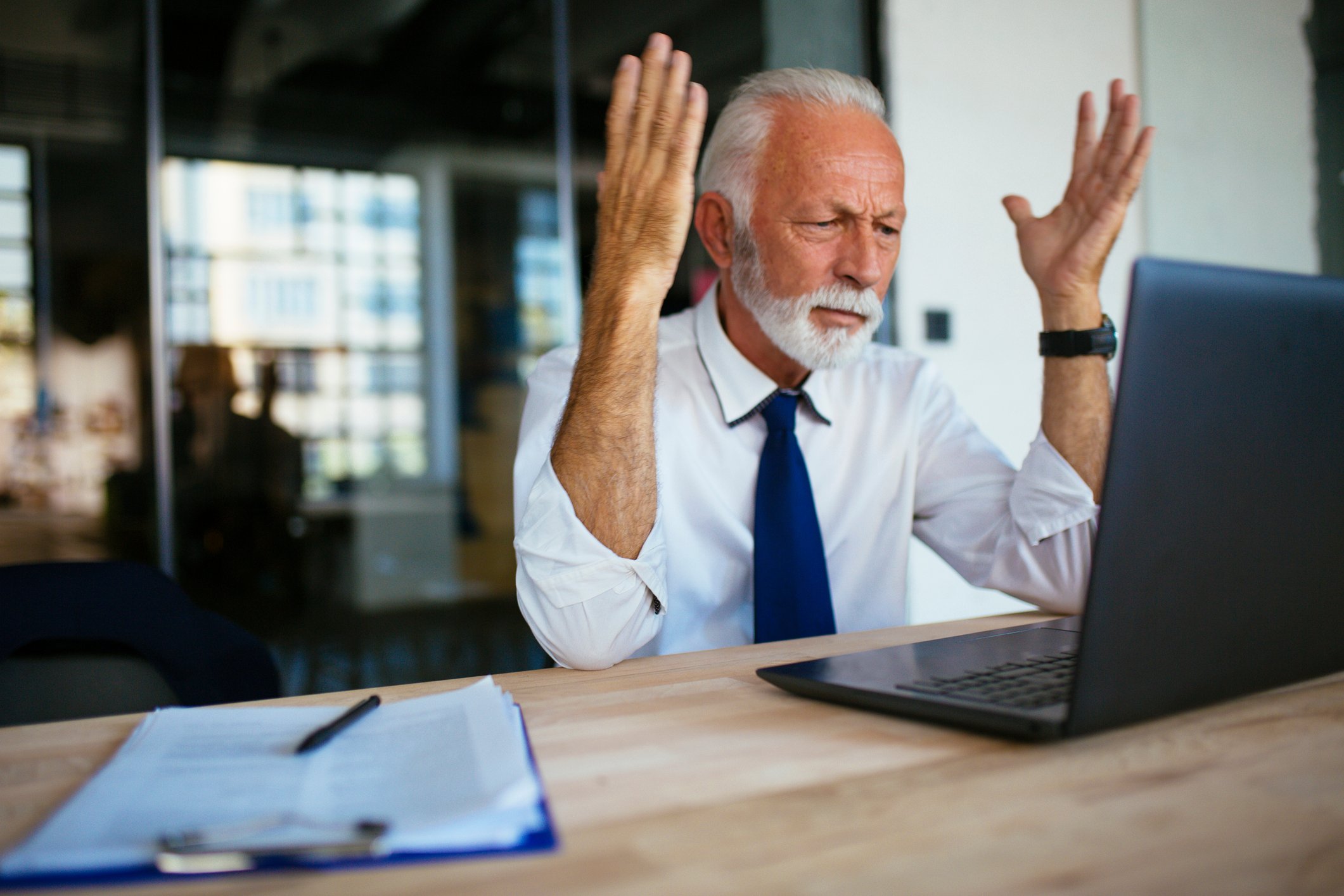 A person at a laptop raising their arms as if angry.
