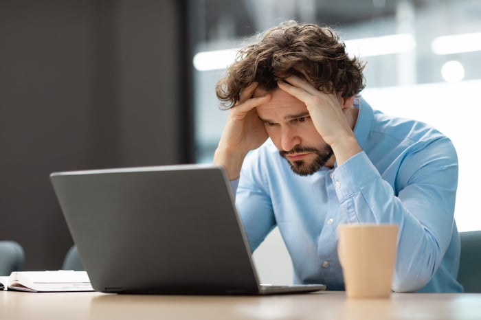 A person at a laptop holding their head.