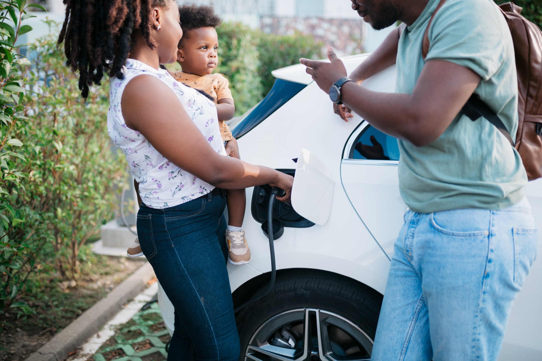 family stands next to a charging electric vehicle.