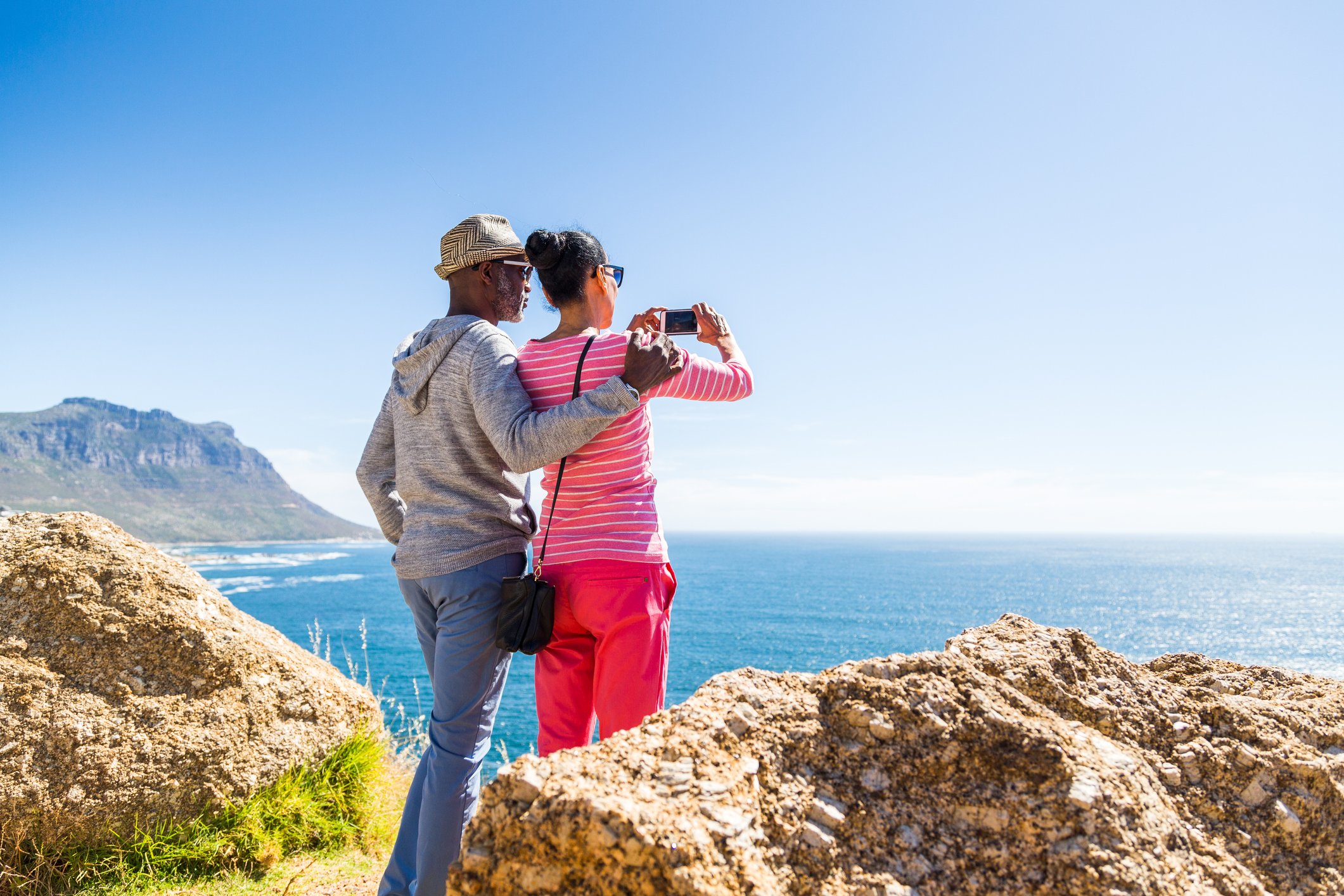 Couple standing on cliff looking out over ocean.