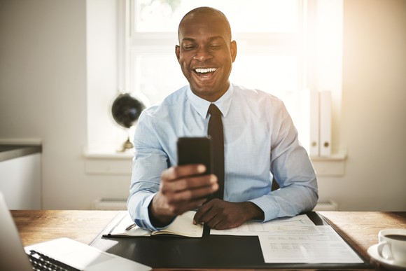 An investor laughs while looking at something on the phone in an office.