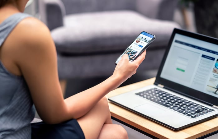 A person holding a smartphone while sitting in front of a computer.