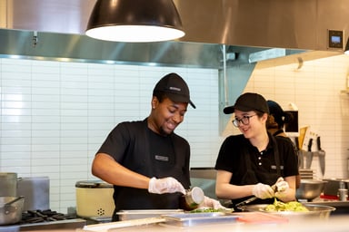 Two smiling Chipotle workers preparing food
