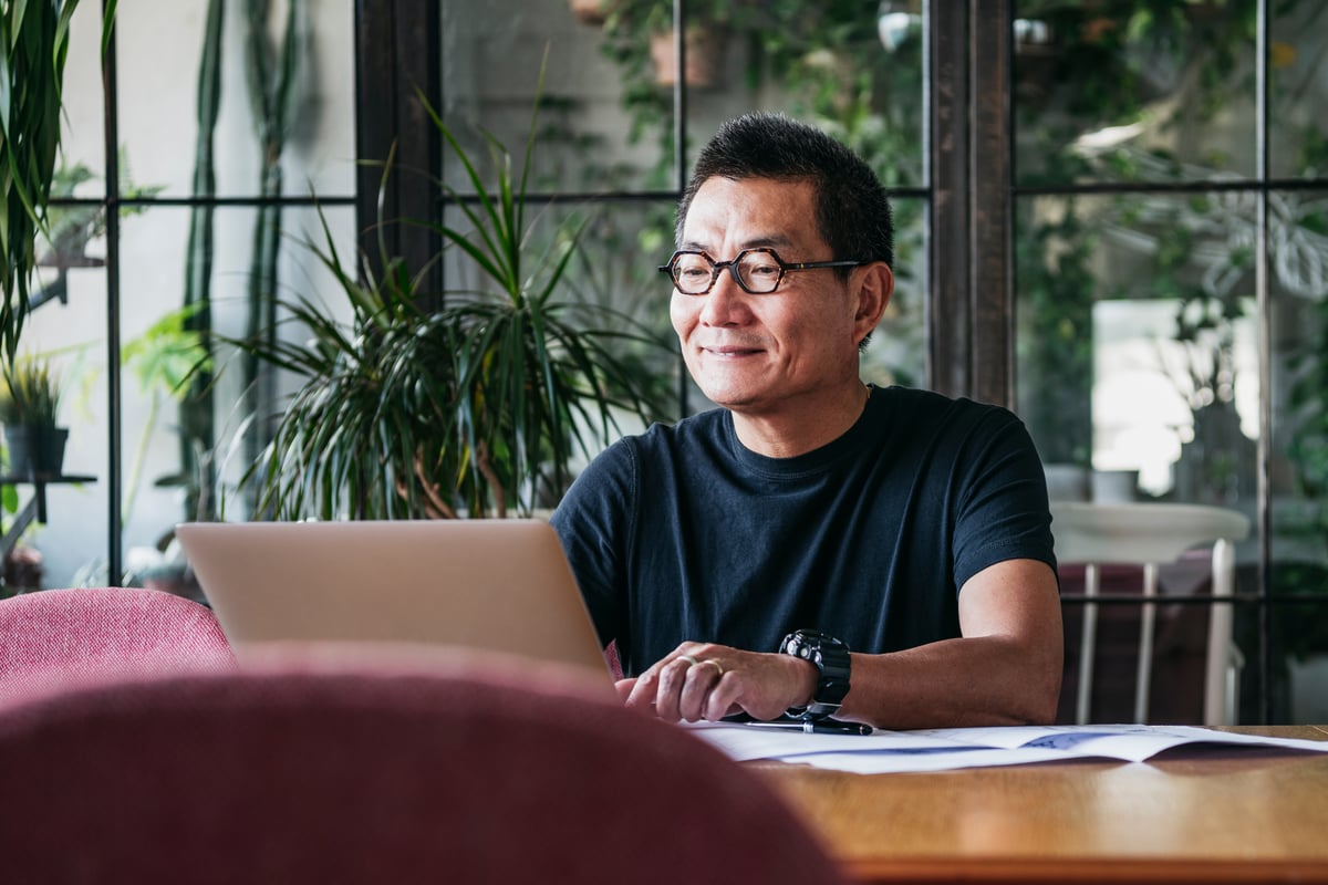 A person sitting at a table smiling while working on a laptop computer. 