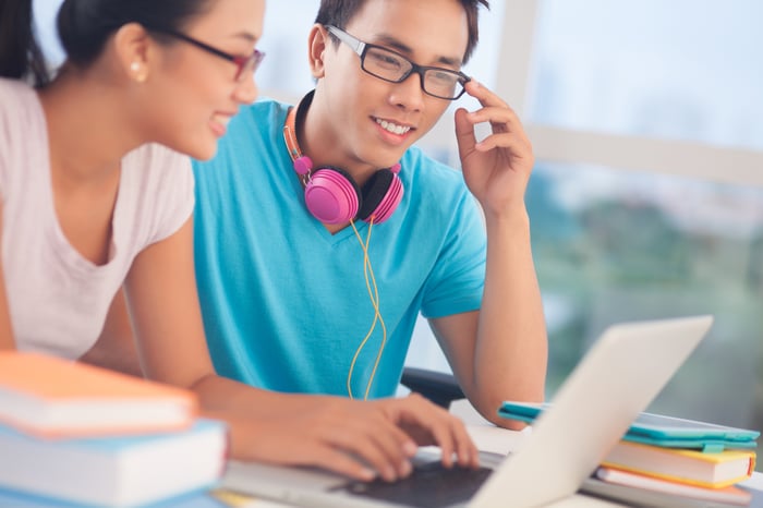 Two college students reading content on a shared laptop.