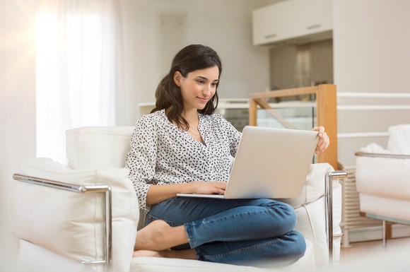 A person sitting on a chair with a laptop computer. 