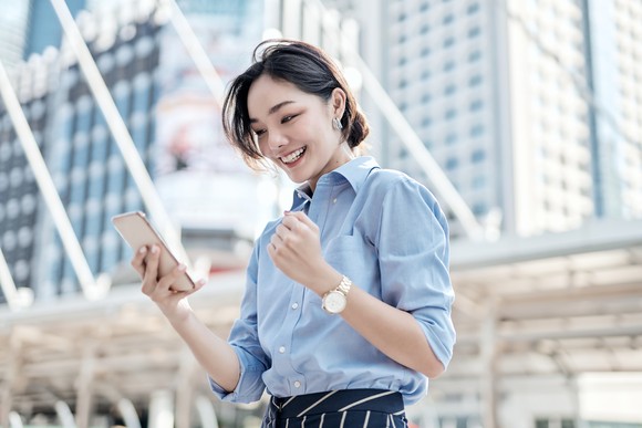 A person smiling while looking at their phone in an urban setting.
