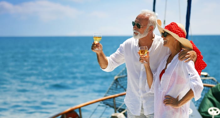 Two seniors toast with drinks while looking out at the sea on a yacht.