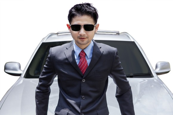 A man in a suit sitting on the hood of a car.