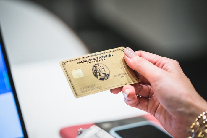 A person holds a gold American Express business credit card in his right hand.