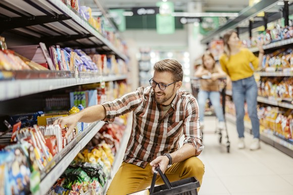Person putting items in basket in store aisle.