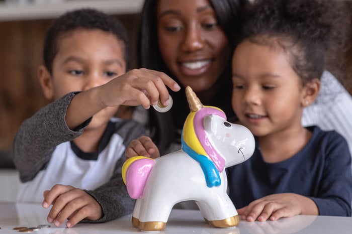 A family puts coins into a piggy bank shaped like a unicorn.