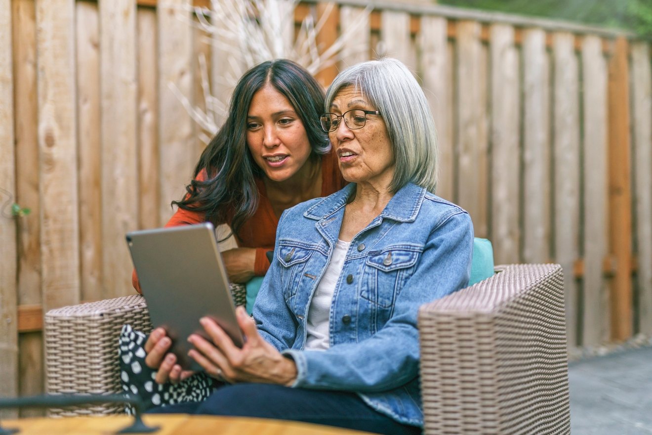Two people sitting outdoors looking at tablet.