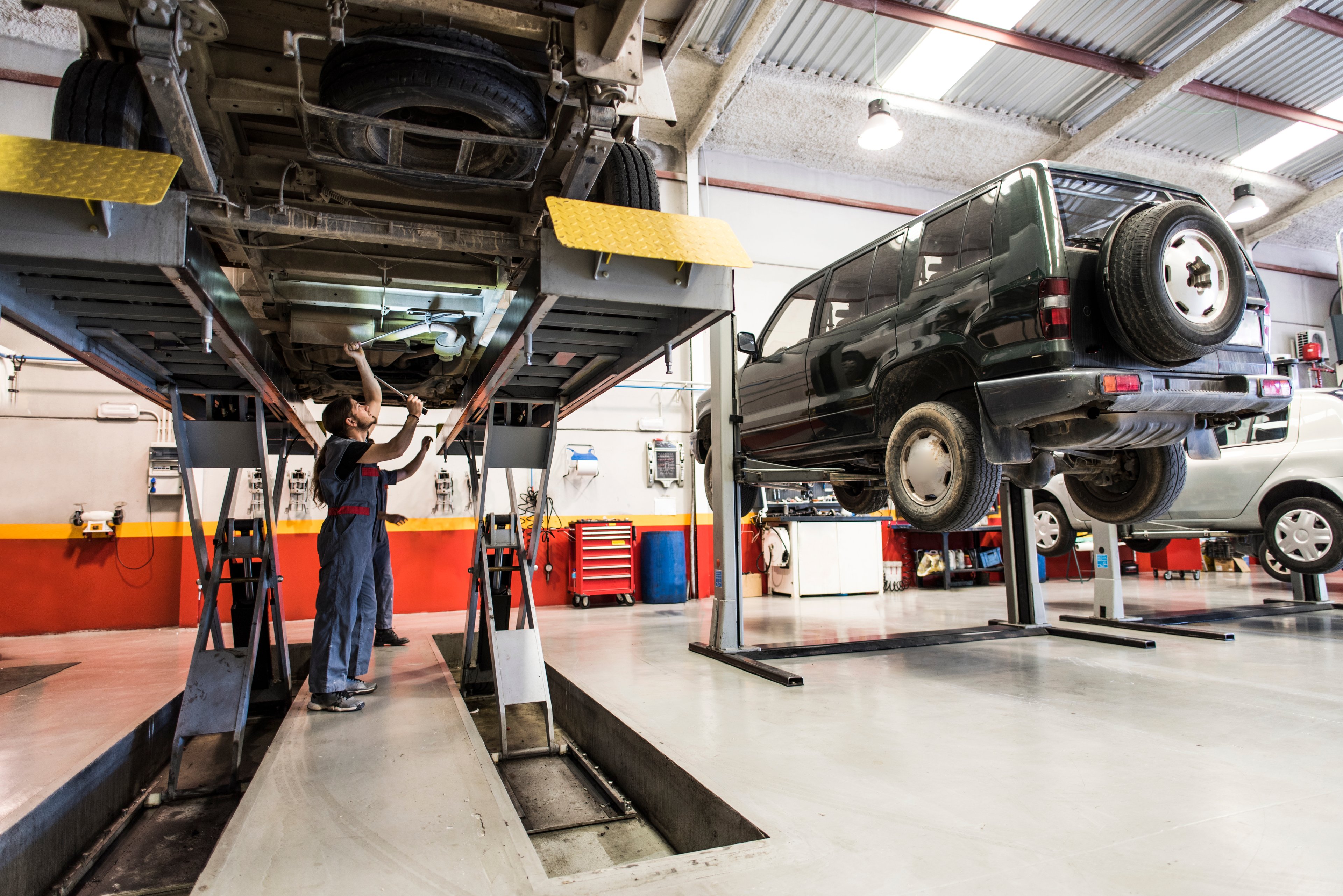 Mechanic works on the underside of a car while it is on a lift.