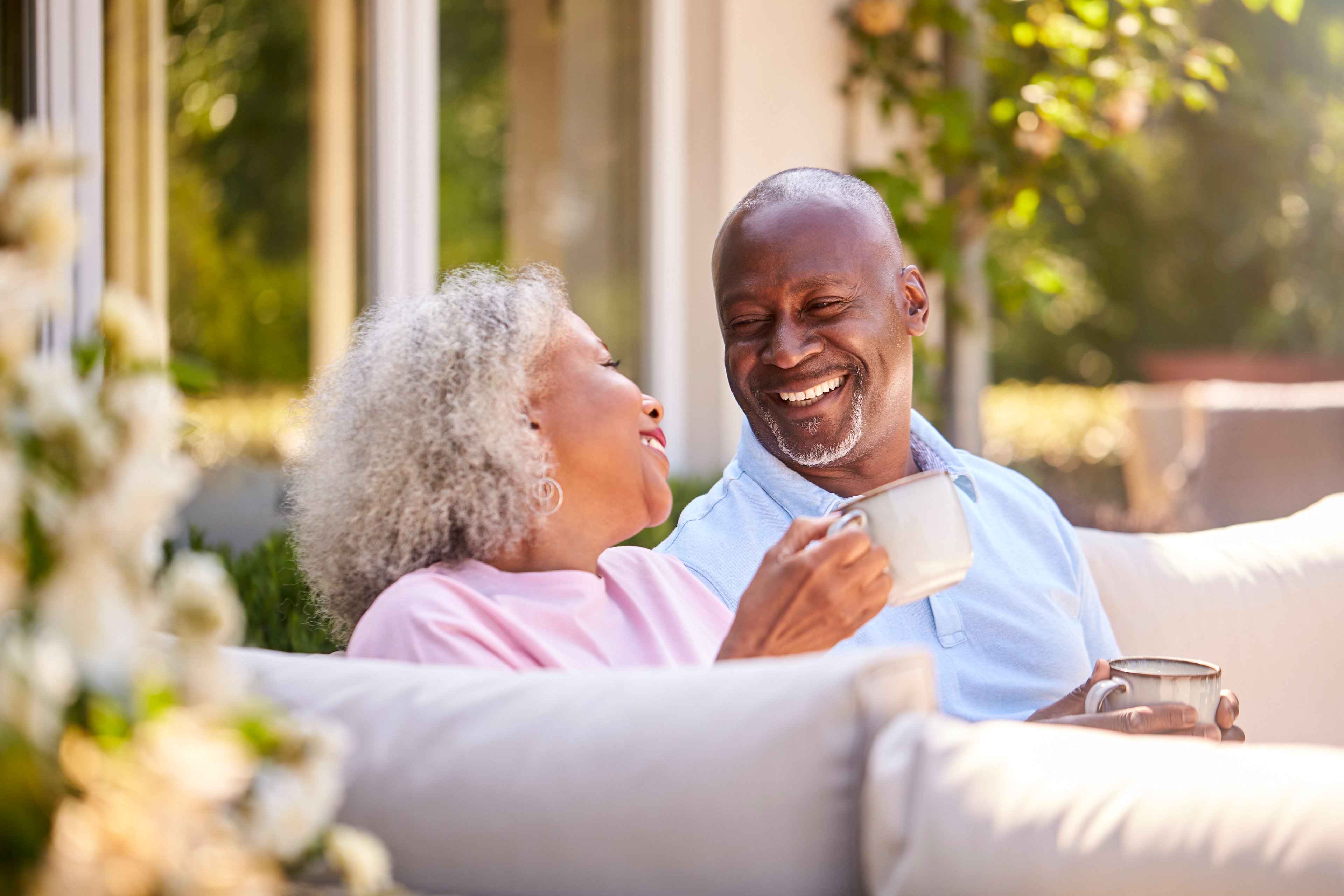 Two people sitting on a couch smiling and holding coffee mugs.