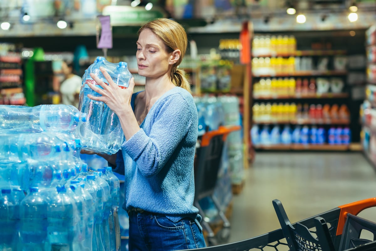 A person lifts a six pack of water bottles off of a pallet at a store. 