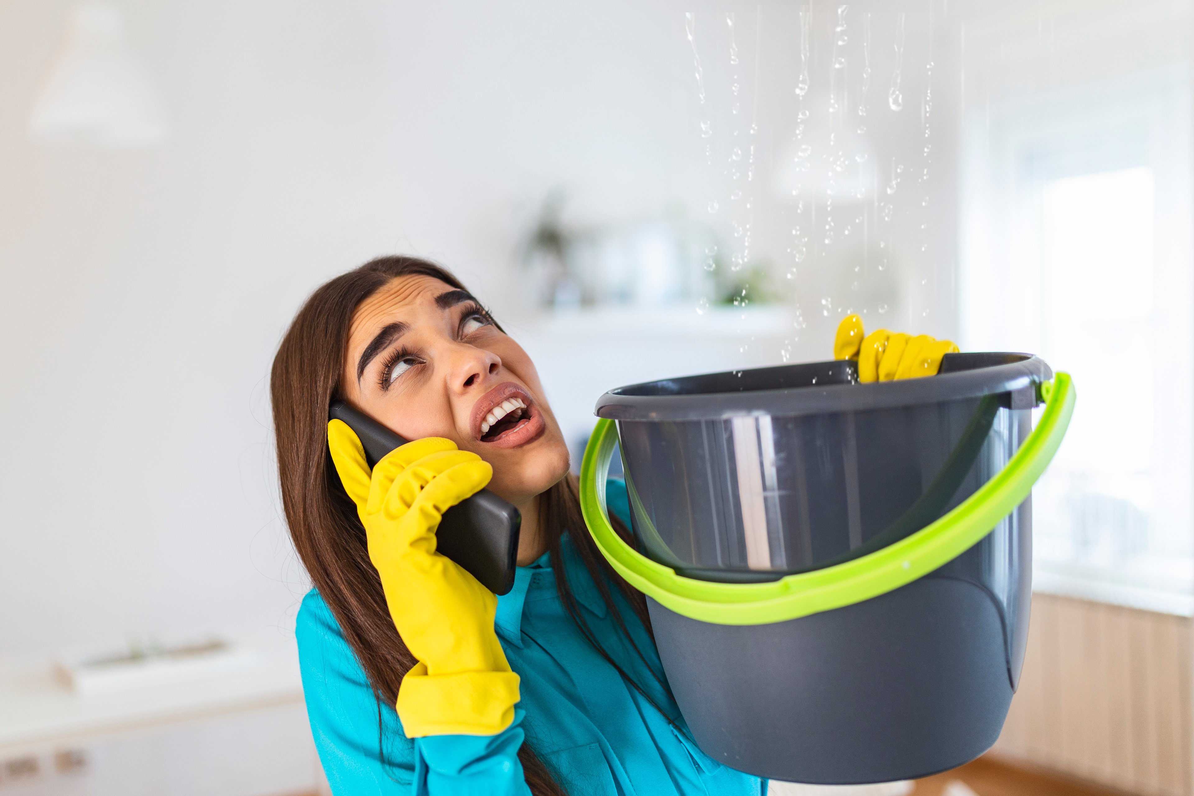 Woman on phone holding bucket for leak in ceiling. 