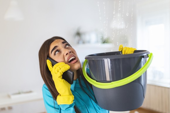 Woman on phone holding bucket for leak in ceiling. 