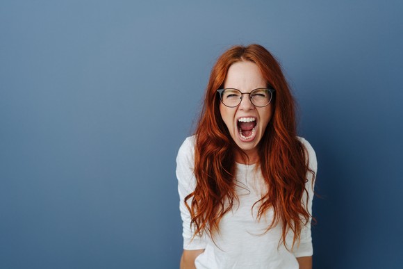 Angry woman yelling in front of a blue backdrop