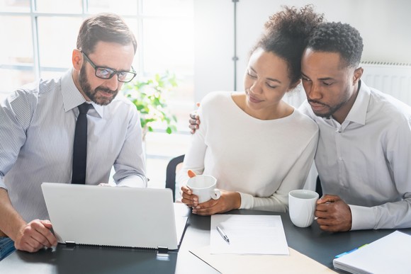 A financial advisor points at a computer while a couple watches.