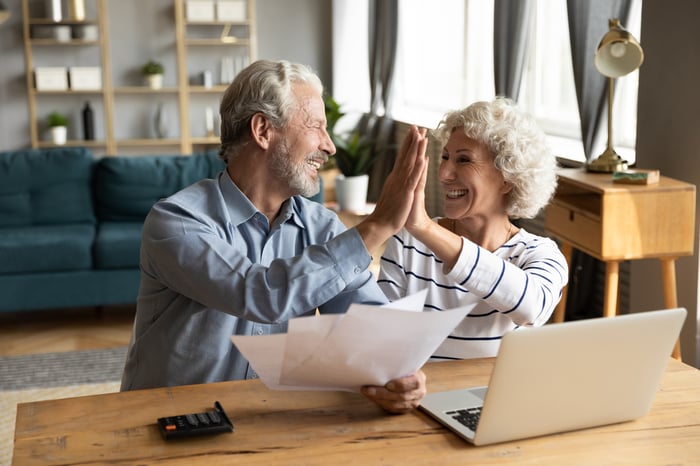 A couple giving each other a high-five while sitting at a table reviewing documents.