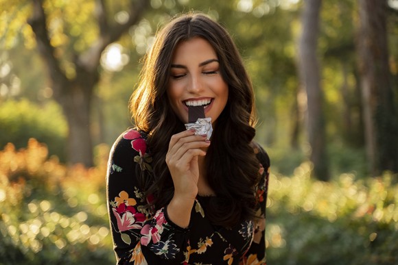 A person takes a bite of a candy bar while visiting a park.