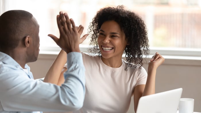 Two smiling people high-fiving over a laptop.