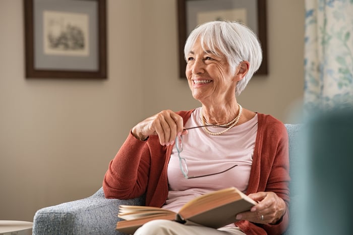 A smiling person sitting in a chair holding a book.