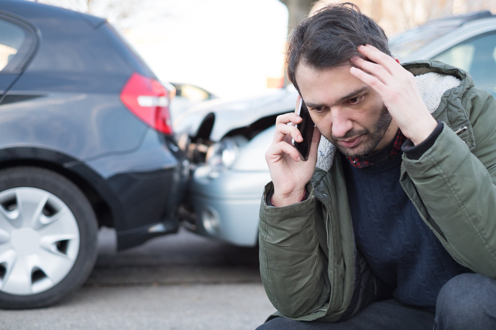 A person on their phone in front of a fender bender car accident.
