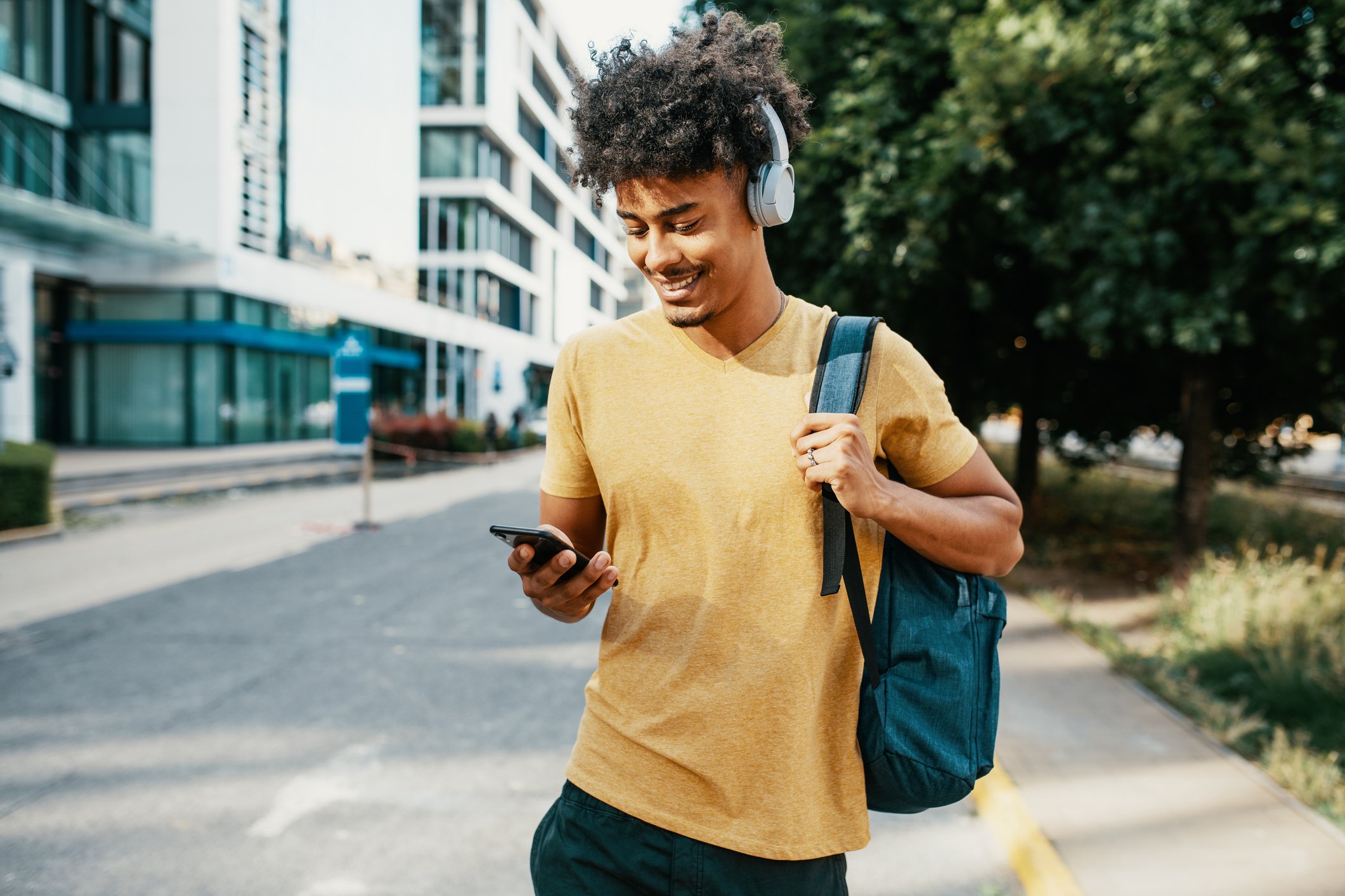 Person on street wearing headphones and looking at smartphone.