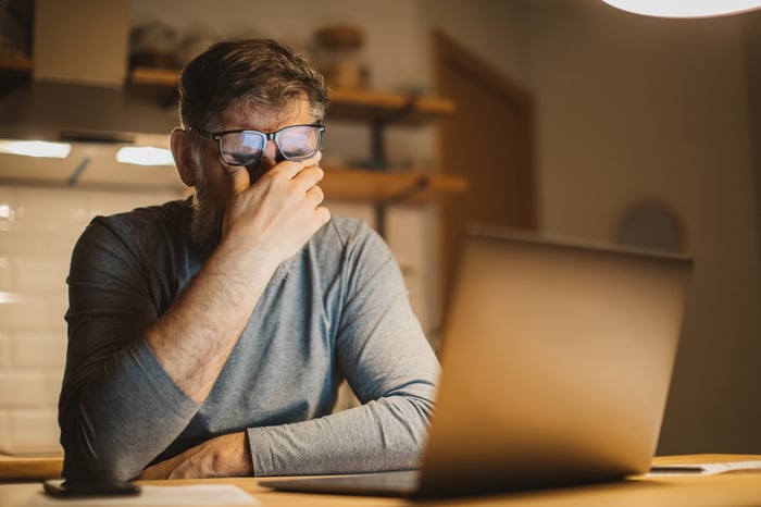 A person at a laptop covering their eyes.