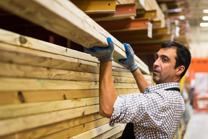 Hardware store employee lifts a plank of lumber.