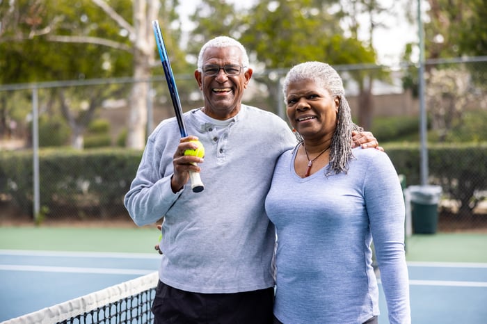 Two people hugging on a tennis court while one holds a tennis racket and ball.