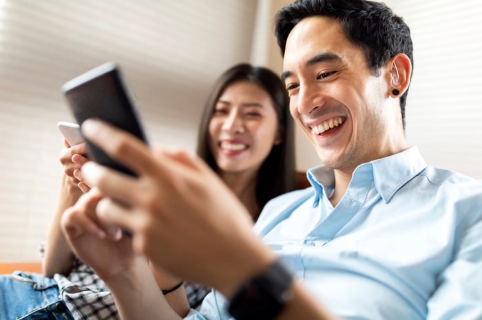 A couple is seated and smiling, looking at a phone.