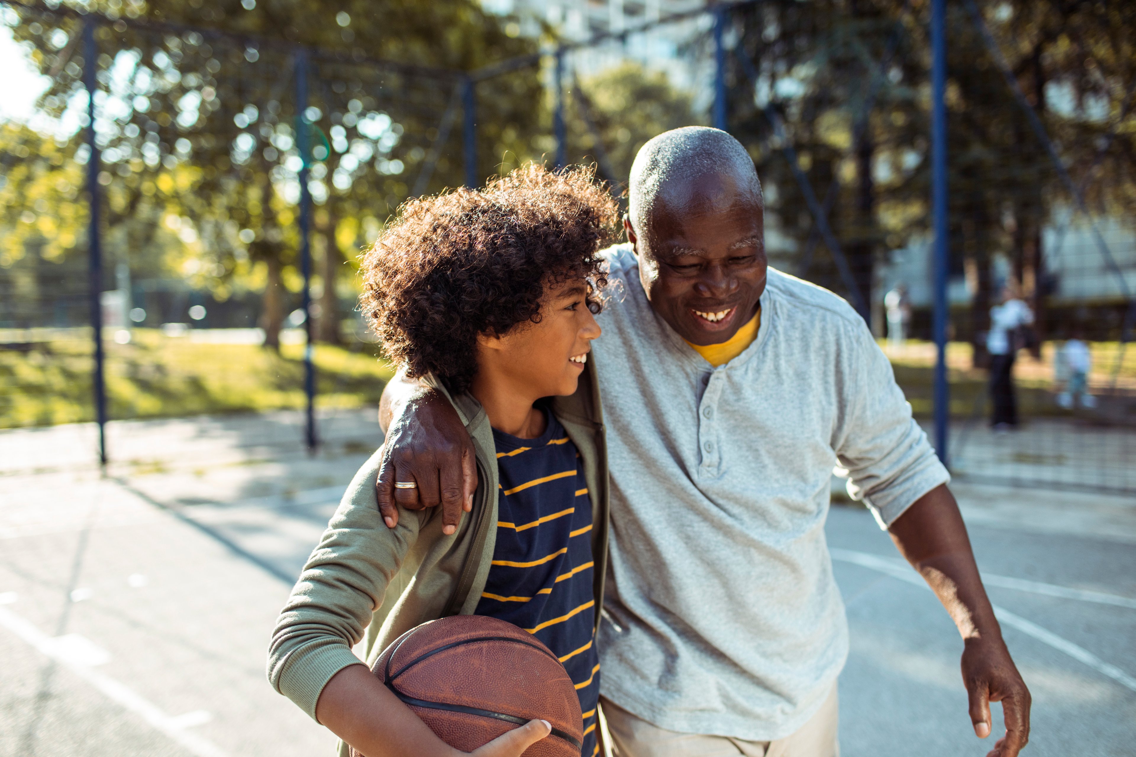 An older person walking beside a younger person holding a basketball. 