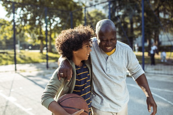 An older person walking beside a younger person holding a basketball. 