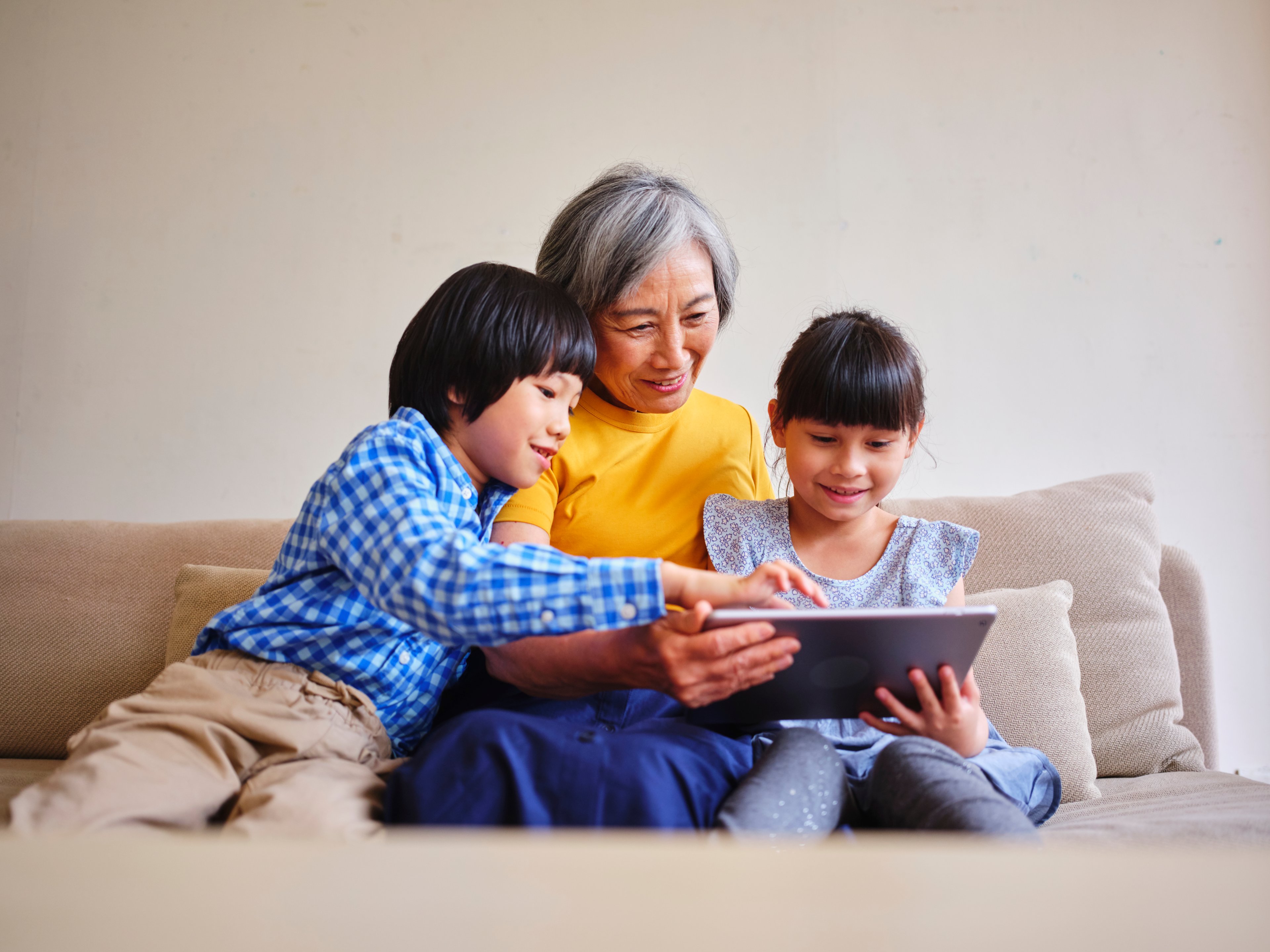 Three people sitting on a couch and looking at a tablet.