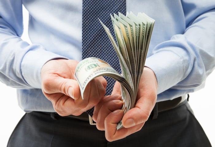 A businessperson rifling through a stack of one hundred dollar bills in their hands. 