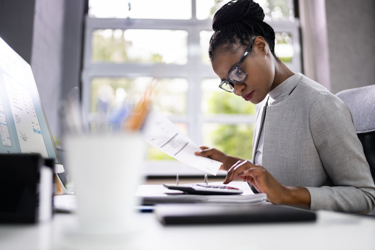 A person sitting at a table and typing on a calculator and holding a piece of paper.