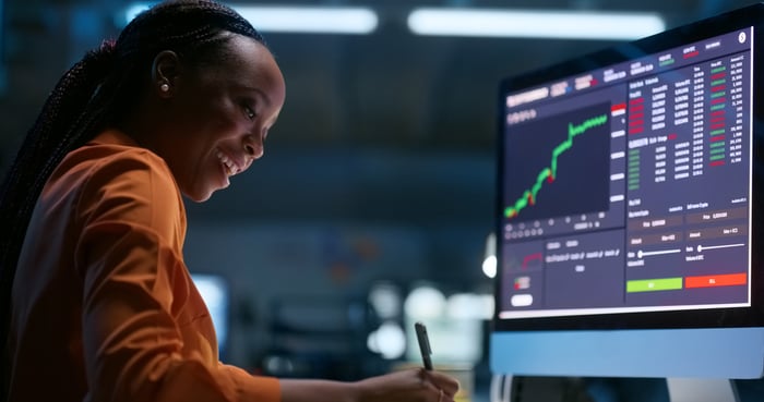 A happy investor looking at a stock price chart on a computer screen and taking notes.