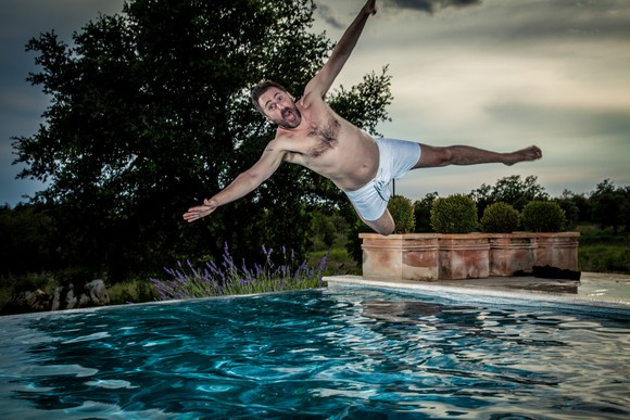 A man jumps sideways into pool. 
