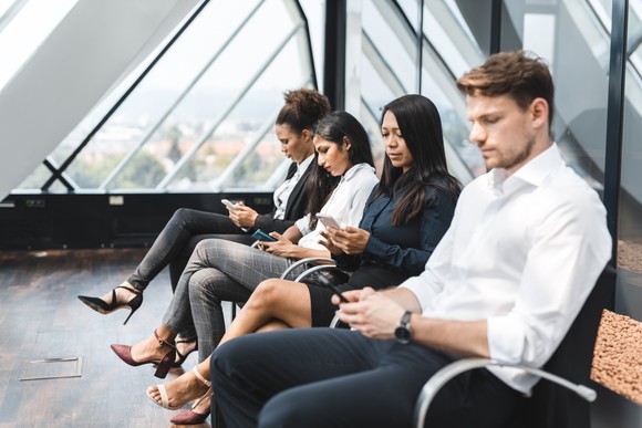 Four people on their phones sitting in a waiting room.